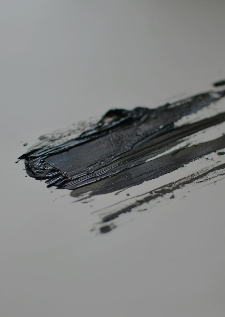 Close-up of a textured black paint streak on a smooth canvas surface.